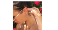 A woman adjusting her sunglasses while wearing earrings and a necklace, surrounded by vibrant flowers.