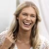 A smiling woman with long blonde hair and a delicate necklace, showcasing joy and elegance in a natural setting.