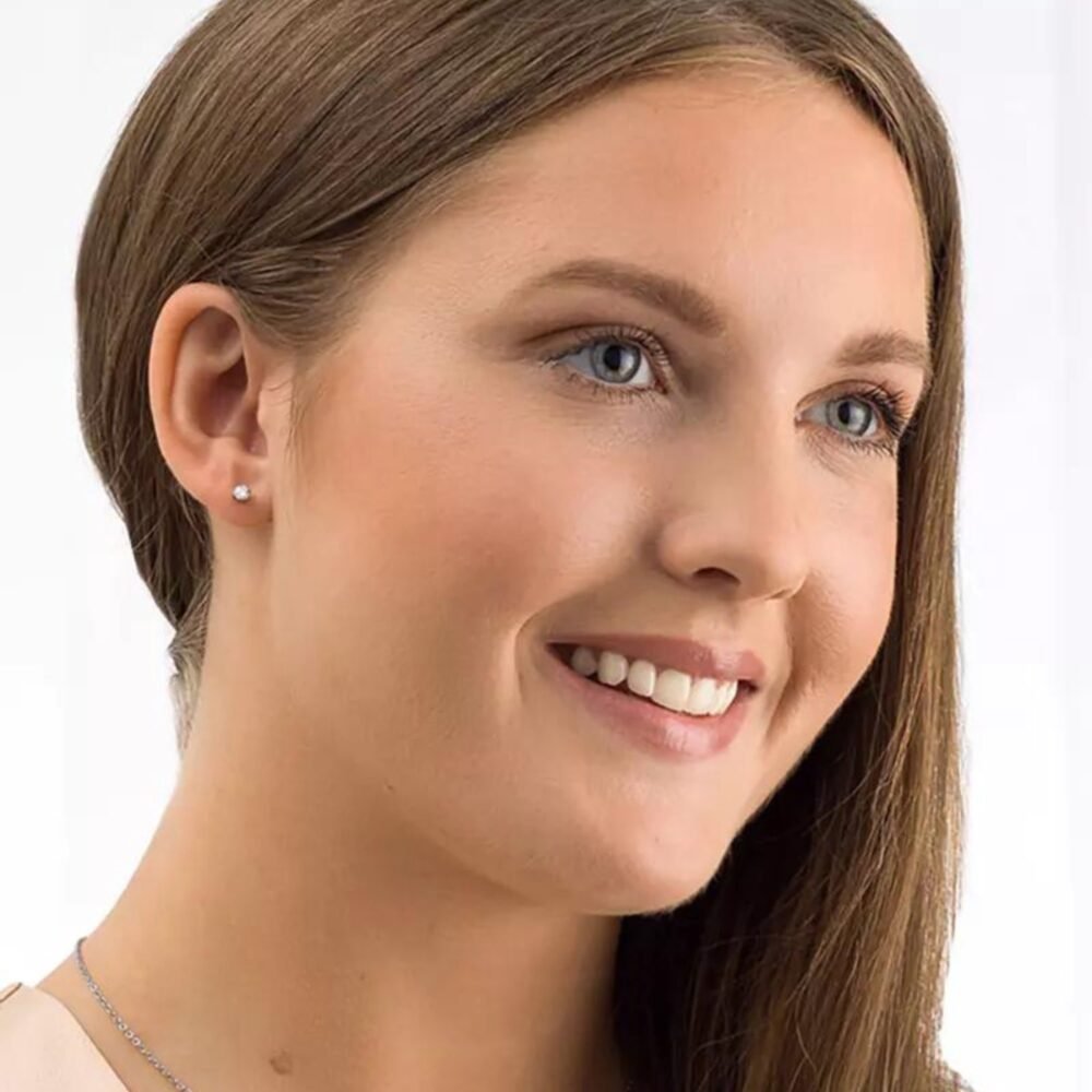 Close-up image of a woman smiling, showcasing her earrings and necklace, highlighting facial features and jewelry details.