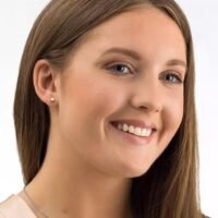 A smiling woman wearing pearl earrings and a delicate necklace, showcasing a natural and elegant look. Her hair is long and straight.