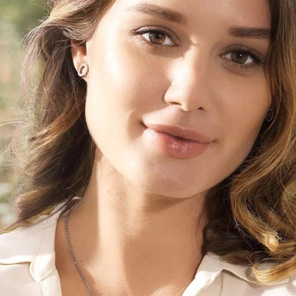 Close-up image of a woman with brown hair and earrings, showcasing a natural beauty look and soft makeup, highlighting facial features.