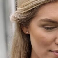 Close-up of a woman wearing elegant diamond stud earrings, showcasing their sparkle and design against her blonde hair.