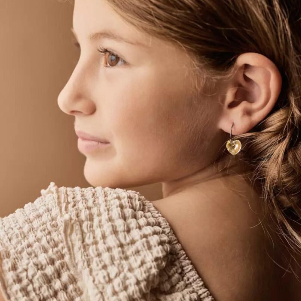 A young girl wearing heart-shaped earrings, showcasing a close-up view of the jewelry and her profile with natural lighting.