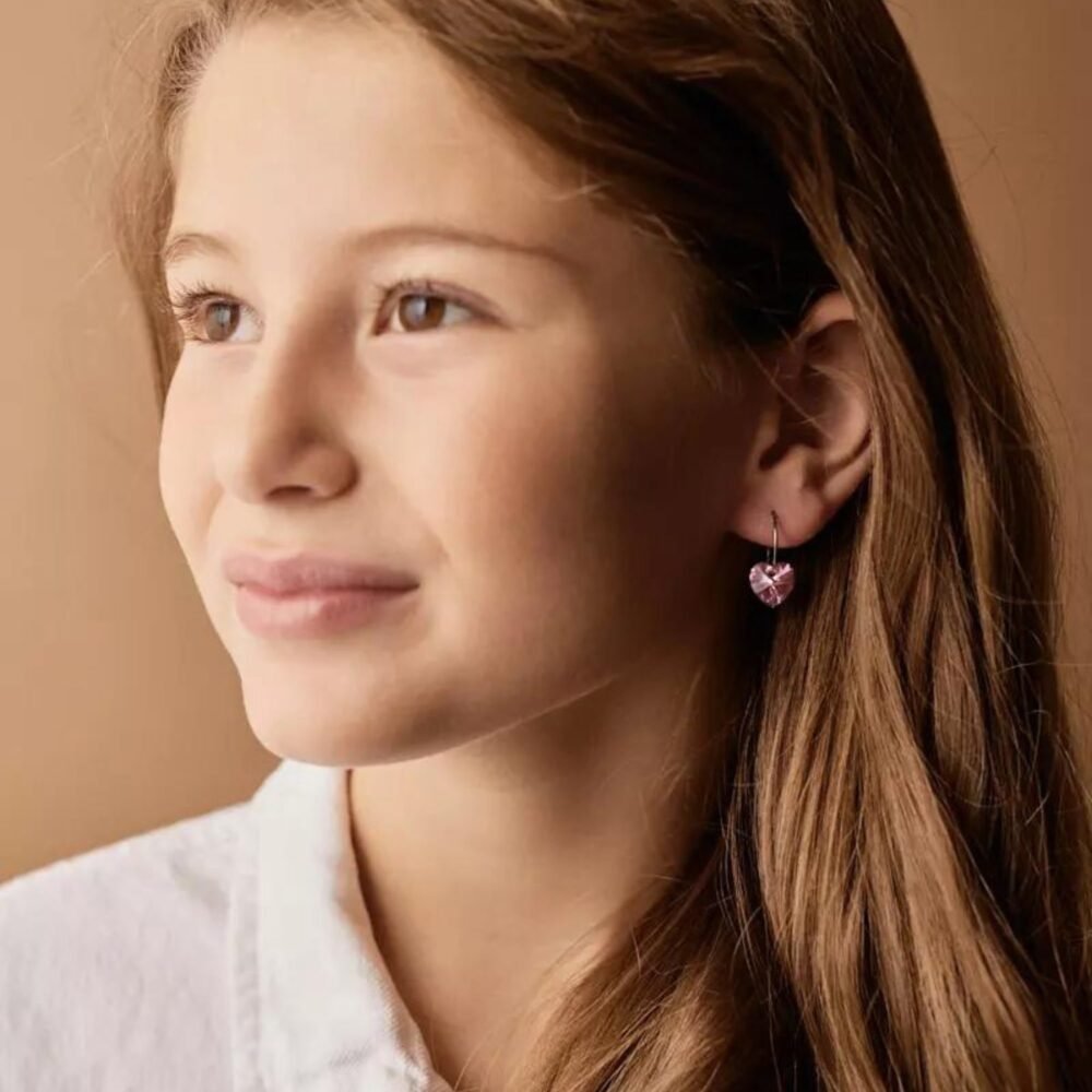 A young girl wearing heart-shaped pink earrings, showcasing a stylish accessory for children. Perfect for adding charm to any outfit.