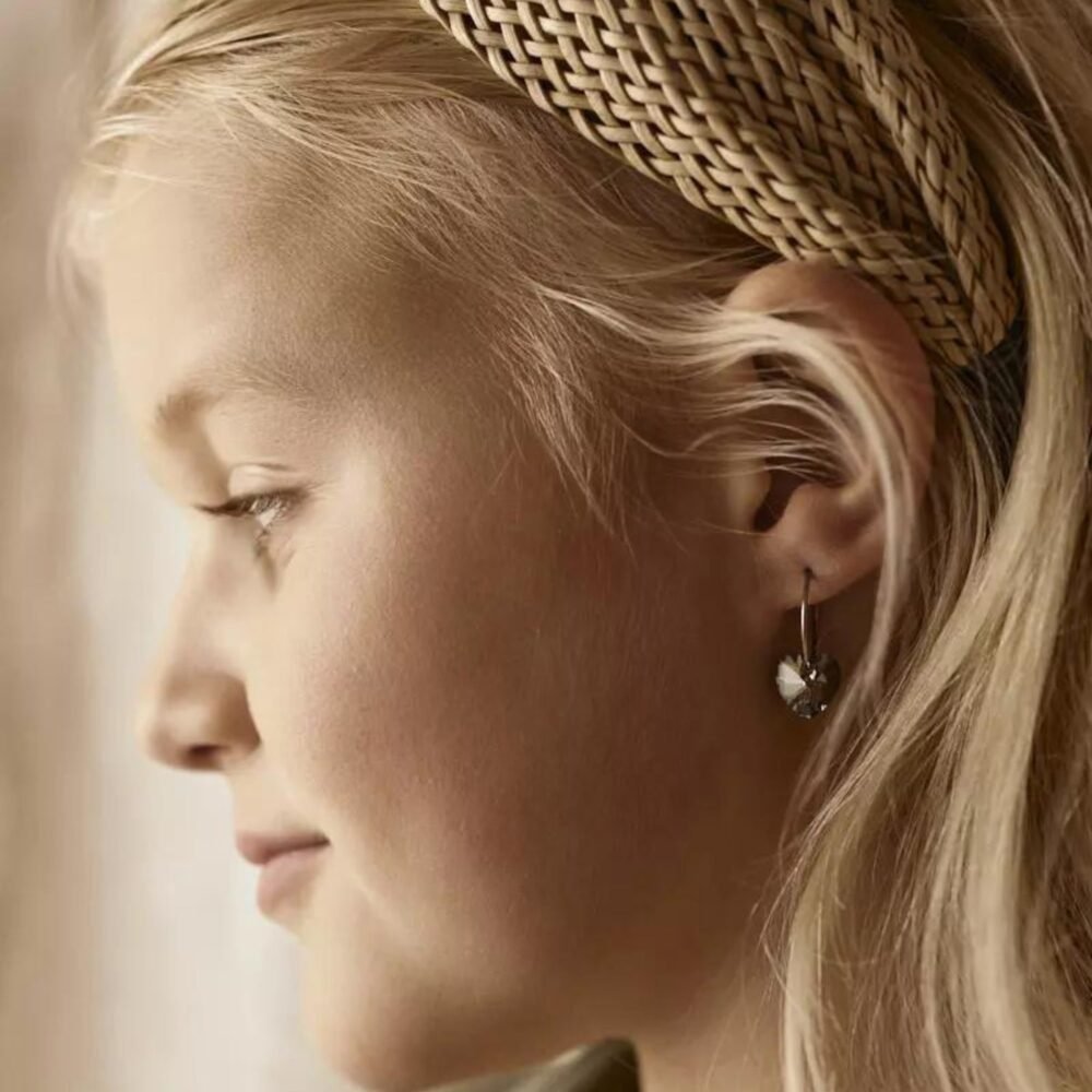 A young girl with blonde hair wearing heart-shaped earrings and a braided headband, showcasing a side profile view.