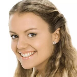 Close-up of a smiling woman with long, wavy hair wearing elegant stud earrings, showcasing a joyful expression and clear skin.