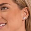 Close-up of a woman wearing elegant diamond stud earrings featuring a round and a smaller stone, showcasing timeless jewelry design.