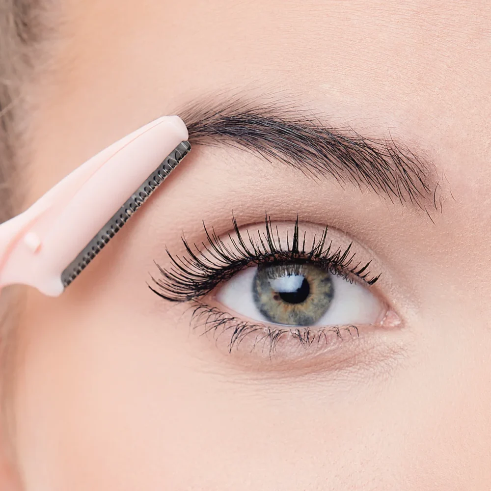 Close-up of a person using a pink eyebrow razor for grooming eyebrows and facial hair, highlighting precision and detail.