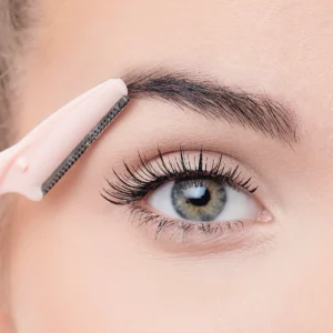 Close-up of a person using a pink eyebrow razor for grooming eyebrows and facial hair, highlighting precision and detail.