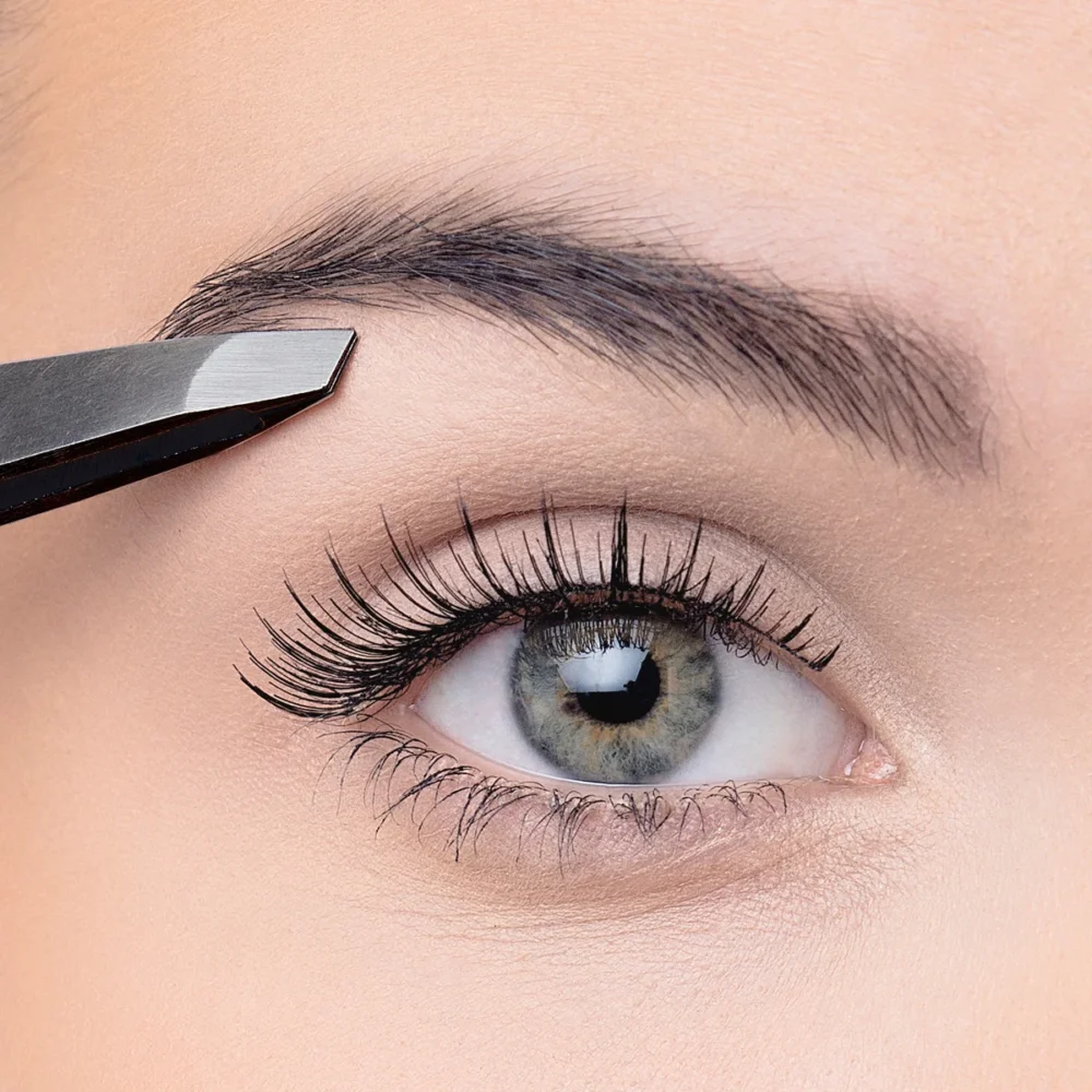 Close-up image of an eye with long eyelashes and tweezers shaping the eyebrow, highlighting beauty and grooming.