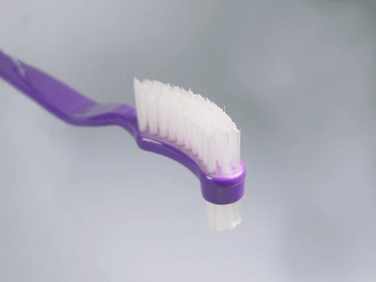 Purple toothbrush featuring a curved design and soft bristles for effective dental care and cleaning.