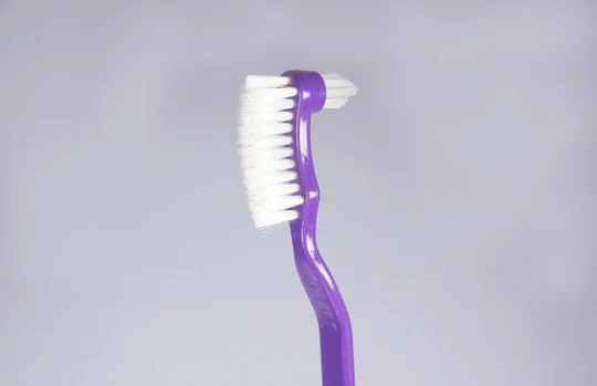 Purple toothbrush featuring a unique angled head and soft bristles for effective cleaning and comfort.