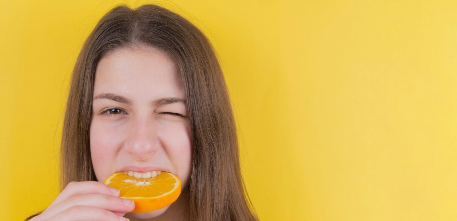 girl holding orange fruit in front of yellow wall