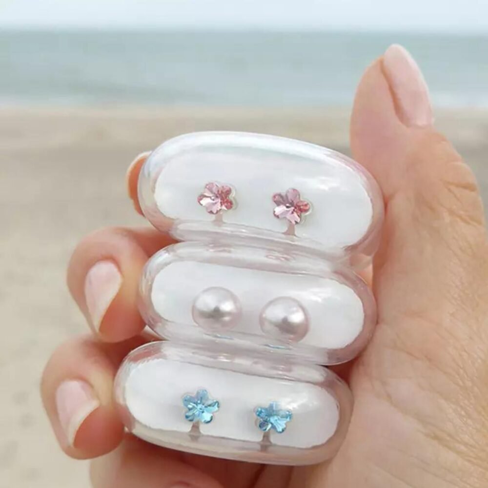 Three pairs of earrings in a clear case, featuring pink flowers, blue flowers, and pearl studs, ideal for jewelry enthusiasts.