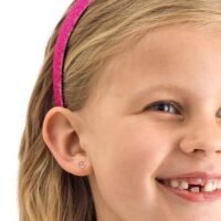 Young girl smiling with a pink headband and stud earrings, showcasing a cheerful expression and playful style.