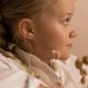 Profile view of a young girl wearing earrings, showcasing delicate jewelry against a soft background.