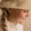 A young girl wearing a straw hat and pink earrings, showcasing a joyful expression. Ideal for jewelry and fashion-related content.