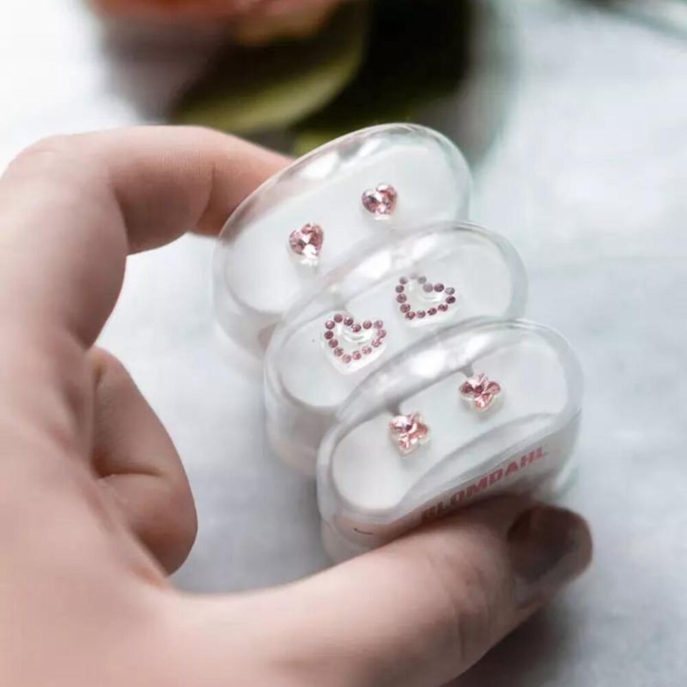 Set of three pairs of pink heart-shaped earrings in clear display case, featuring sparkling stones and a charming design.