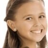 A young girl smiling while wearing heart-shaped earrings, showcasing a joyful expression and light brown hair.