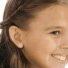 Heart-shaped diamond earrings worn by a smiling girl, showcasing a delicate and charming design suitable for children.