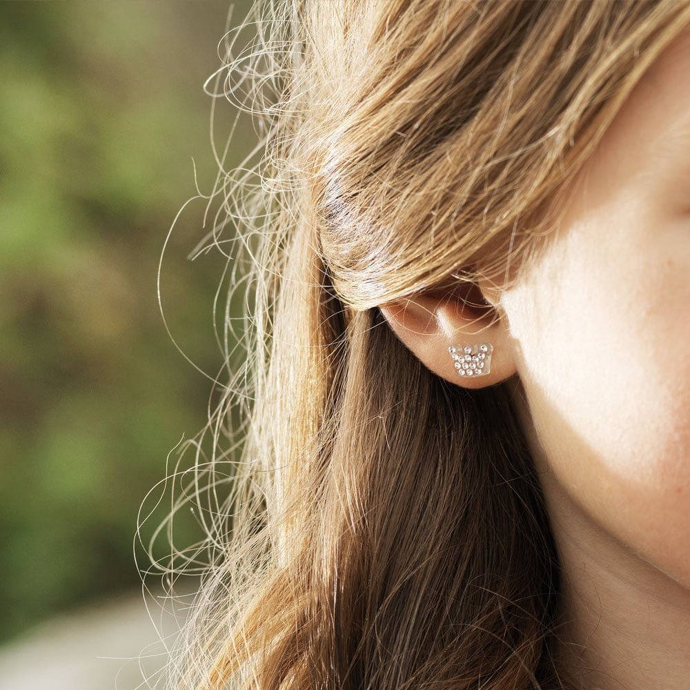 A close-up of a child's ear adorned with sparkling silver earrings, showcasing a delicate design with small gemstones.