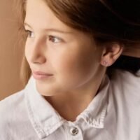 A young girl with light brown hair wearing elegant stud earrings, showcasing a simple yet stylish accessory for children.