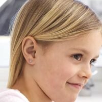 Close-up of a young girl with blonde hair wearing flower stud earrings, showcasing a delicate and stylish accessory for children.