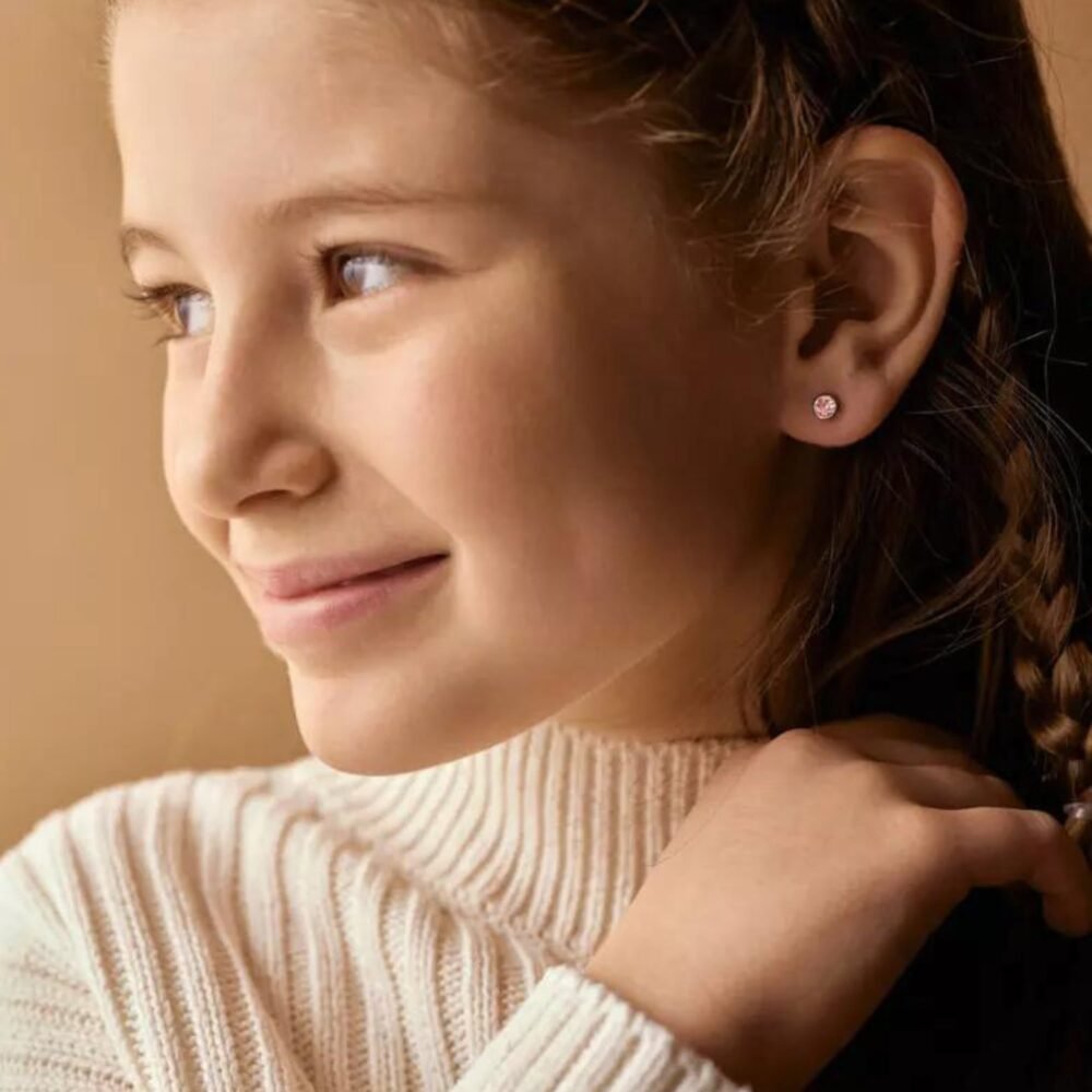 Close-up of a young girl smiling, showcasing delicate stud earrings and a braided hairstyle, with a soft background.