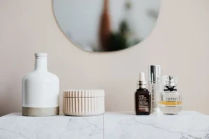 A collection of skincare products and perfumes on a marble surface, featuring a white bottle, cream jar, serum, and two fragrance bottles.