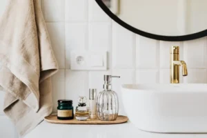 beauty essentials .. Stylish bathroom accessories including a soap dispenser, perfume bottles, and a candle on a wooden tray beside a sink.